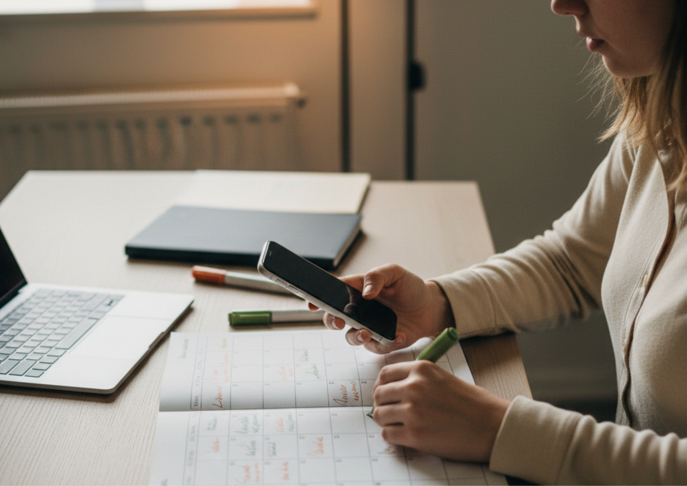 Mulher organizada planejando metas SMART em um calendário físico sobre a mesa, utilizando um smartphone e canetas coloridas para definir objetivos específicos e prazos.